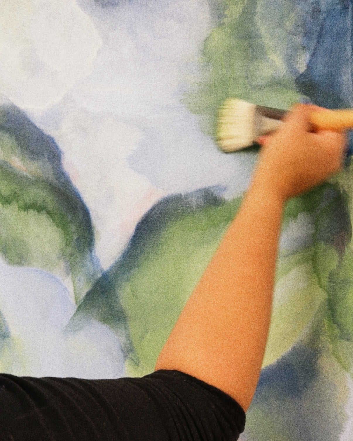 Hand holding a brush over a watercolor landscape painting