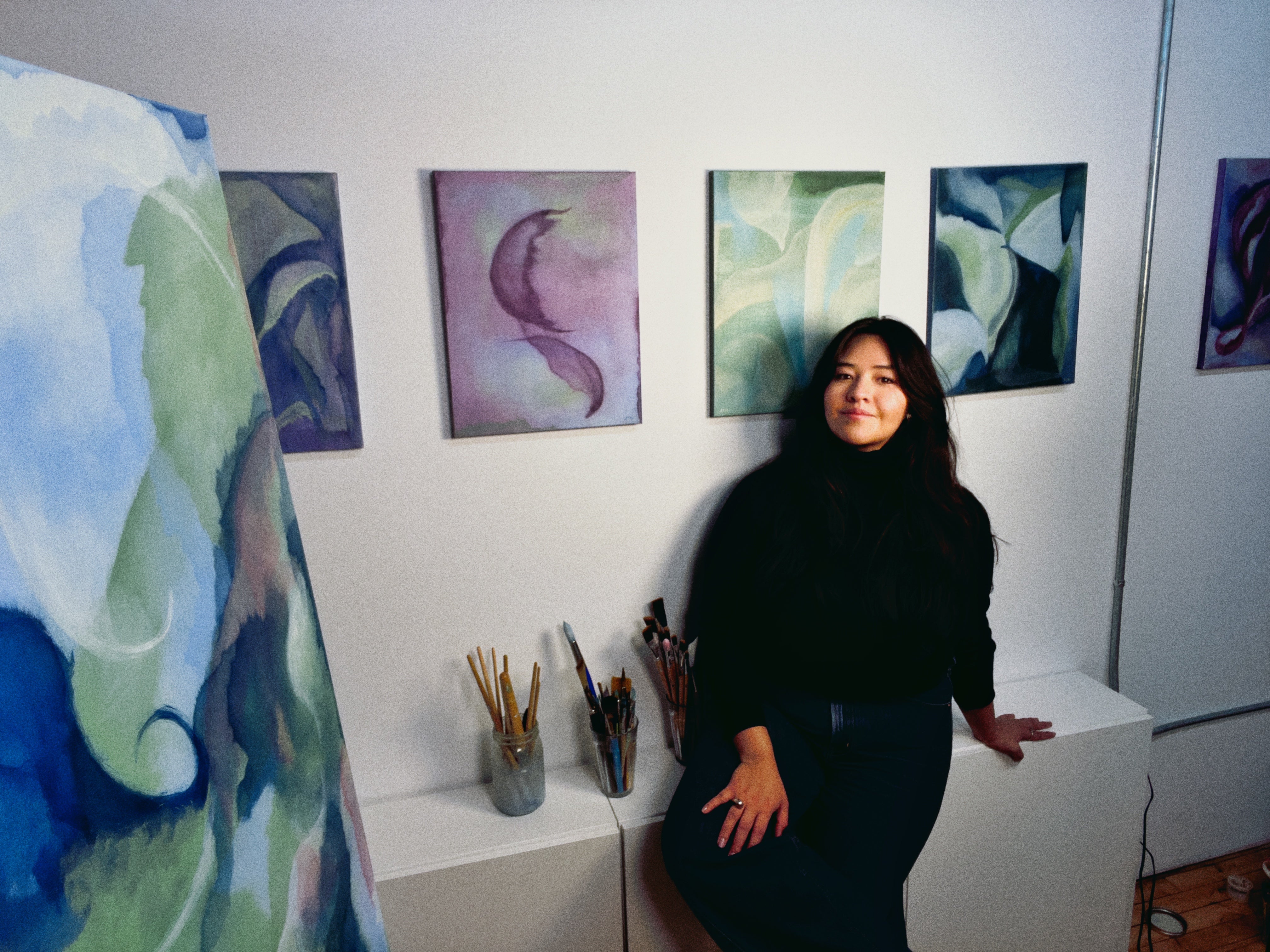 Woman standing in an art studio with various artworks on the wall.