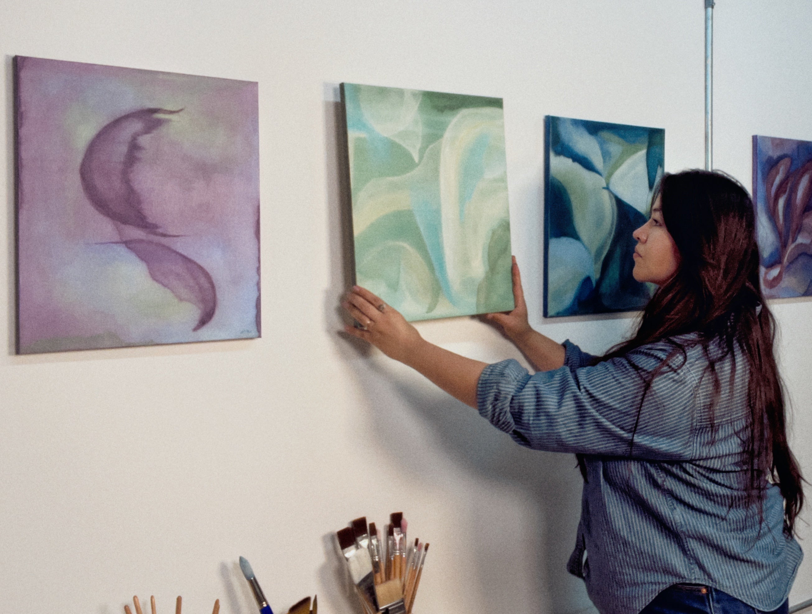 Person arranging abstract paintings on a wall