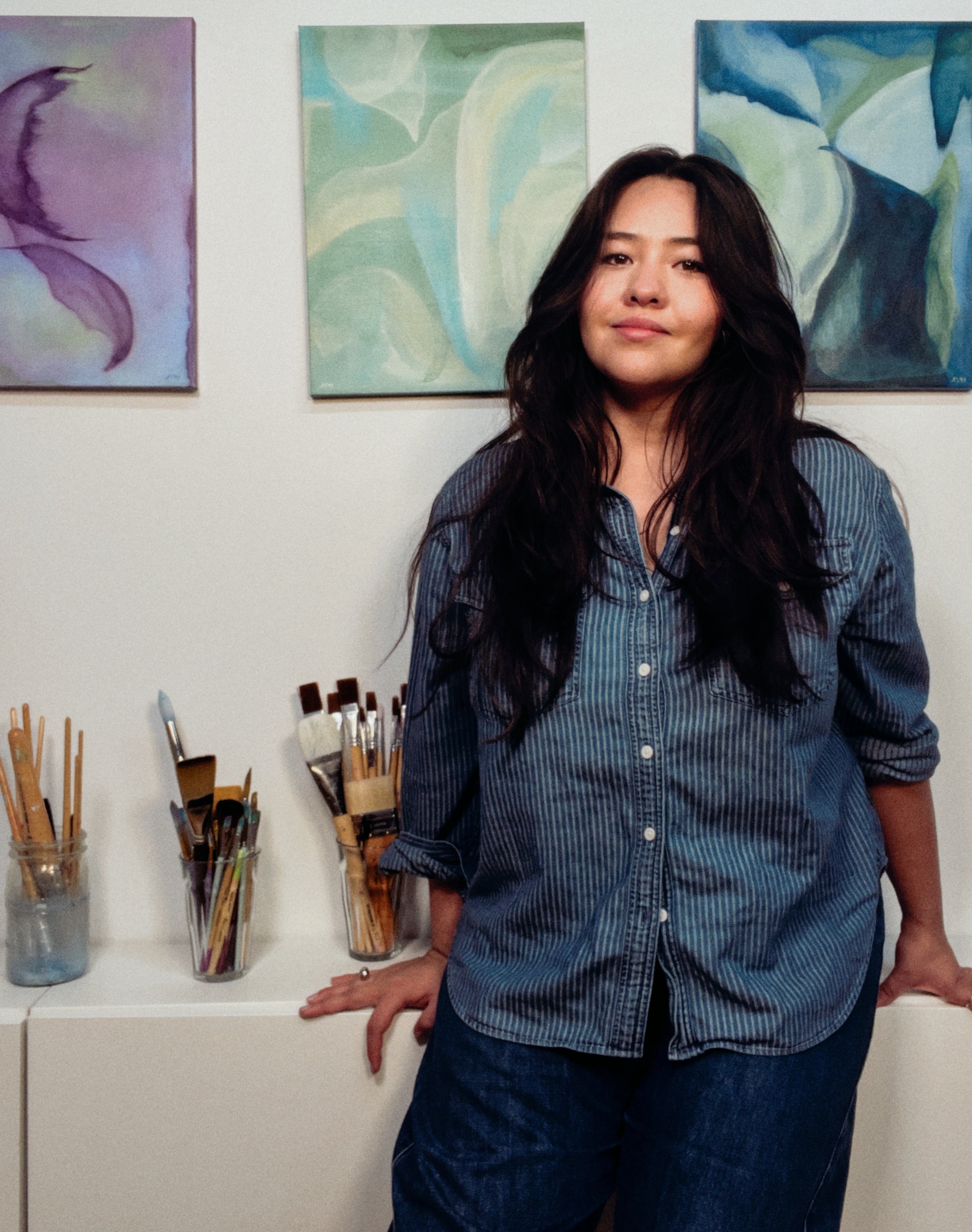 Woman standing in front of abstract paintings in an art studio.