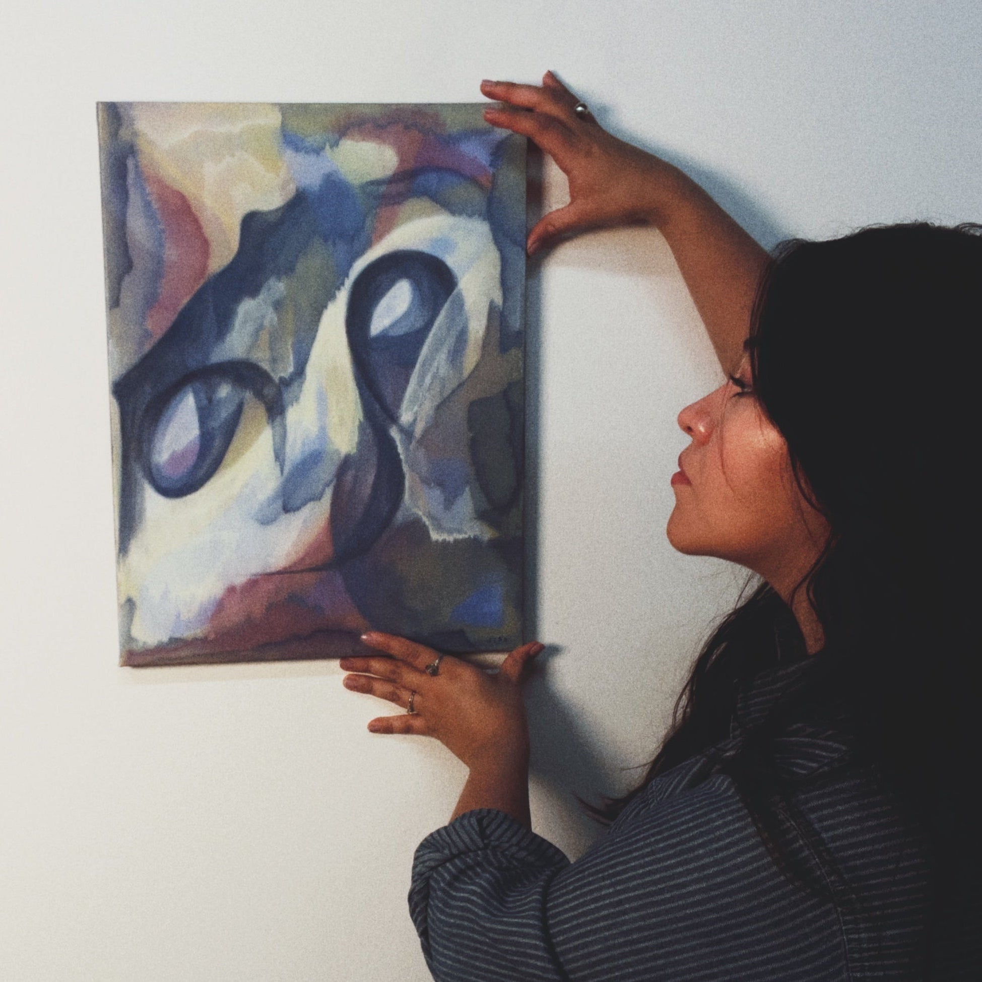 Person adjusting a colorful abstract painting on a wall