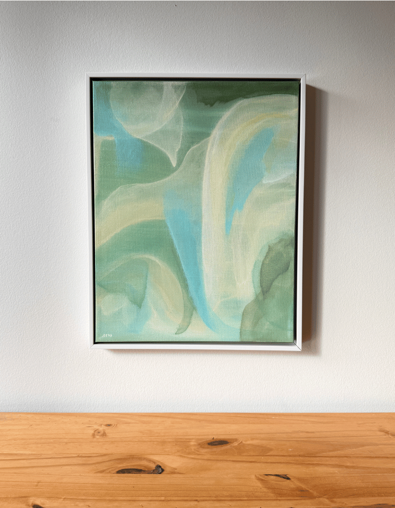 Framed abstract artwork with wavy green and blue patterns on a white wall above a wooden surface.