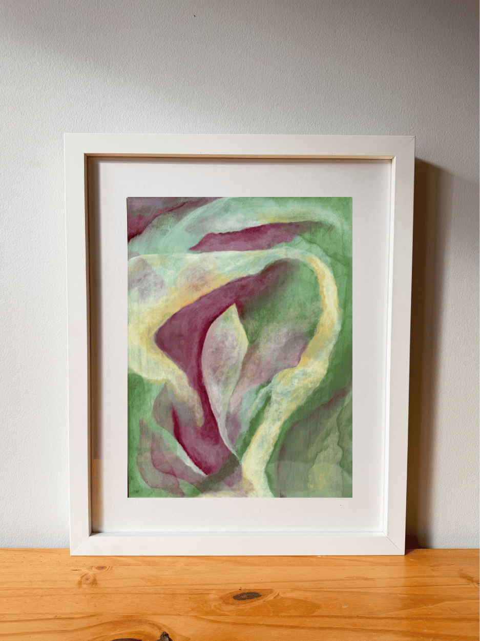 Framed abstract artwork with green and purple hues on a wooden surface.