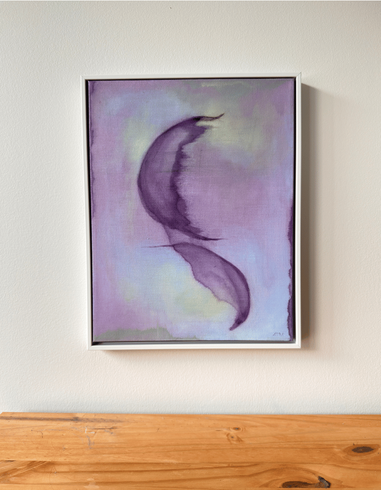 Framed abstract art piece with a purple and pink color scheme on a white wall above a wooden surface.
